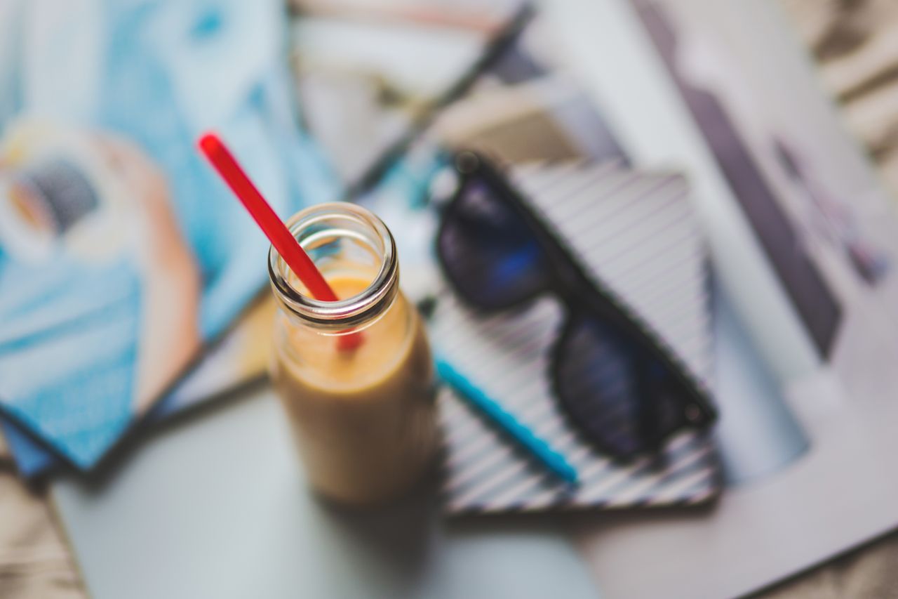 hero-img-02 A refreshing smoothie with red straw on an artistic desk setup featuring sunglasses and stationery.