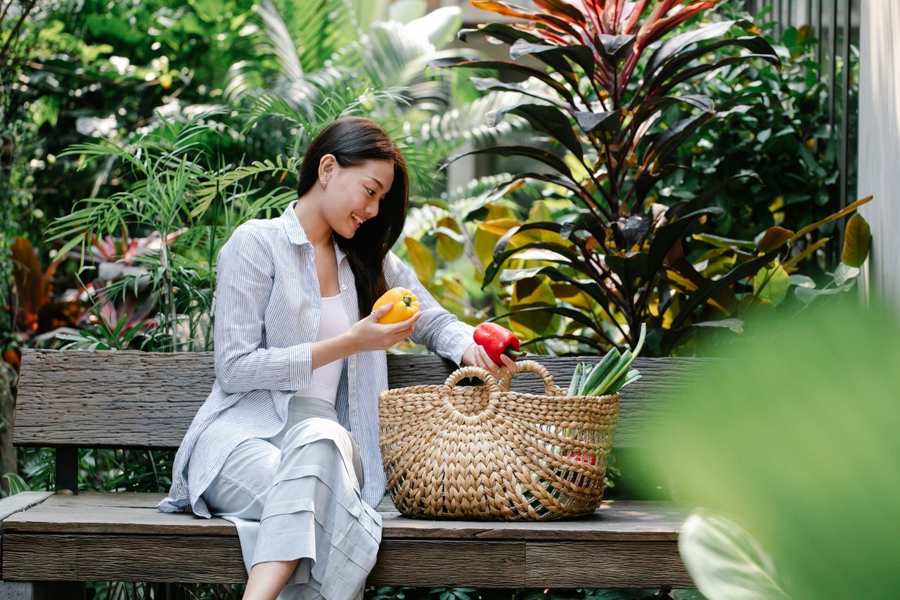 why-choose-us Content Asian female wearing casual outfit placing fresh yummy capsicums in wicker basket while sitting on wooden bench in verdant garden